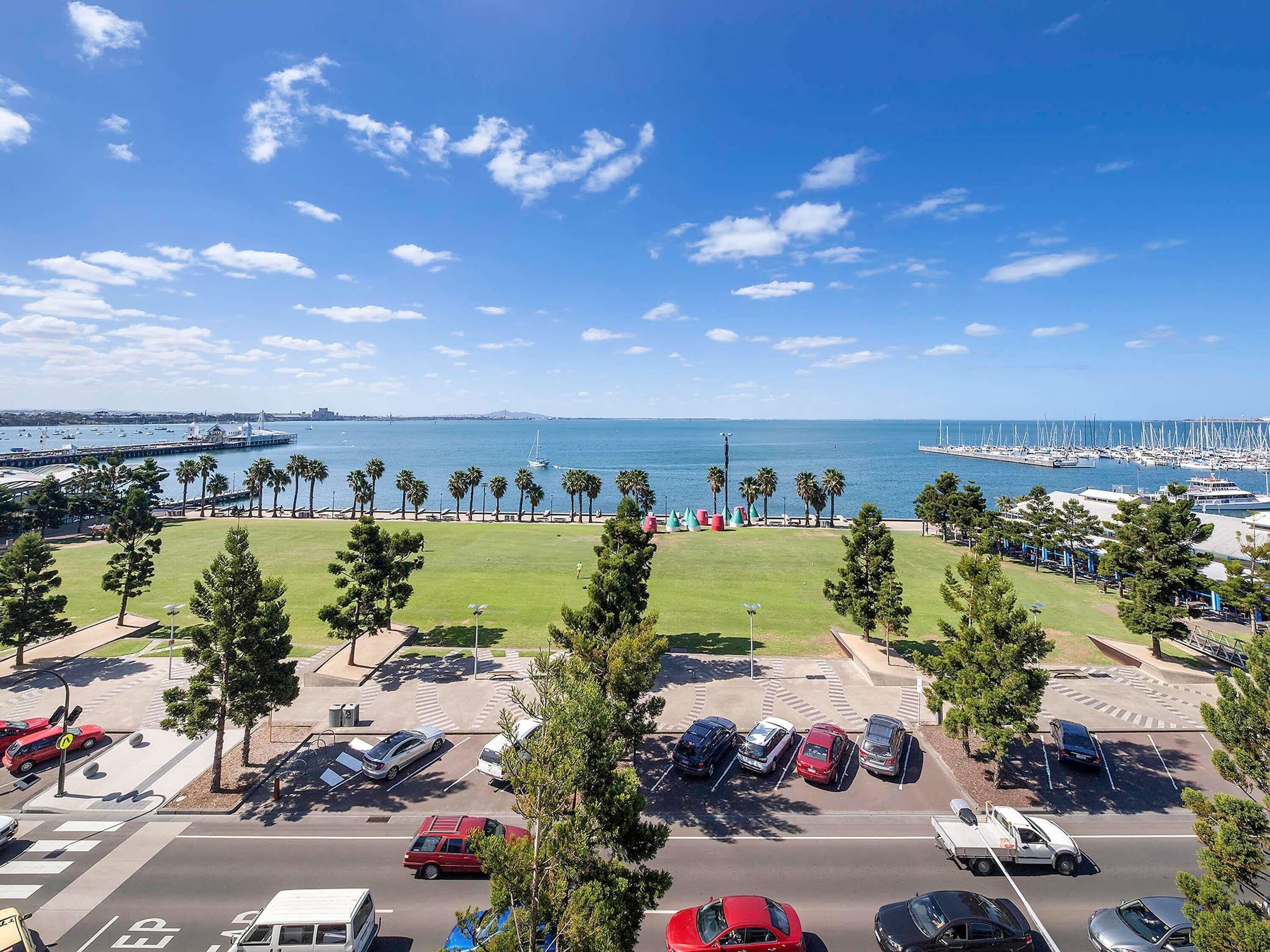 A parking lot with cars, a grassy area, and a marina with boats in the background.