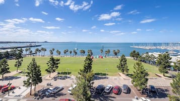 A parking lot with cars, a grassy area, and a marina with boats in the background.