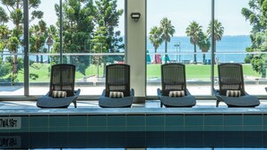 Zona junto a la piscina con tres sillones de mimbre y vista despejada al mar y palmeras.