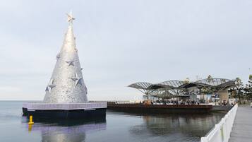 Una gran estructura metálica con forma de árbol de Navidad junto al agua, al lado de un moderno edificio de vidrio con techo curvo.