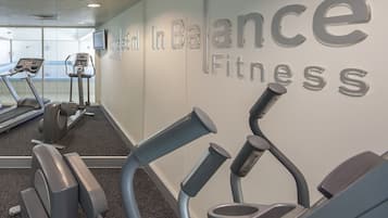 Ein Fitnessraum mit Laufbändern und Crosstrainern, eine Wand mit der Aufschrift 'In Balance Fitness' und ein Schild, das eine 30-minütige Erholungsphase anzeigt.