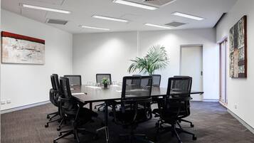 A conference room with a long table, black chairs, a potted plant, and artwork on the walls.