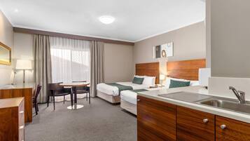 A hotel room with a bed, a desk, a chair, a small table, a sink, and a window with curtains.