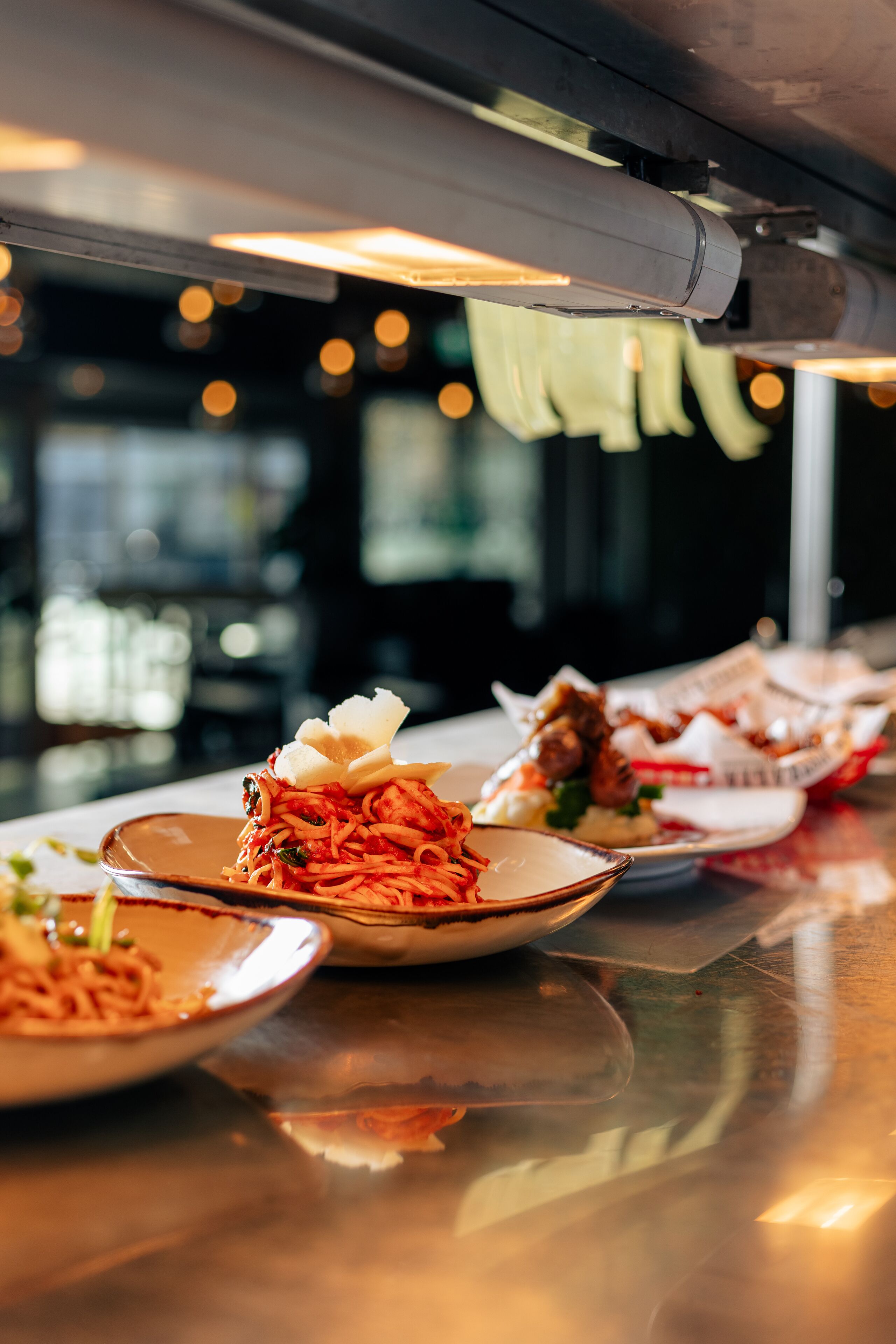 A restaurant counter with various dishes, including pasta and meat, and a reflective surface.
