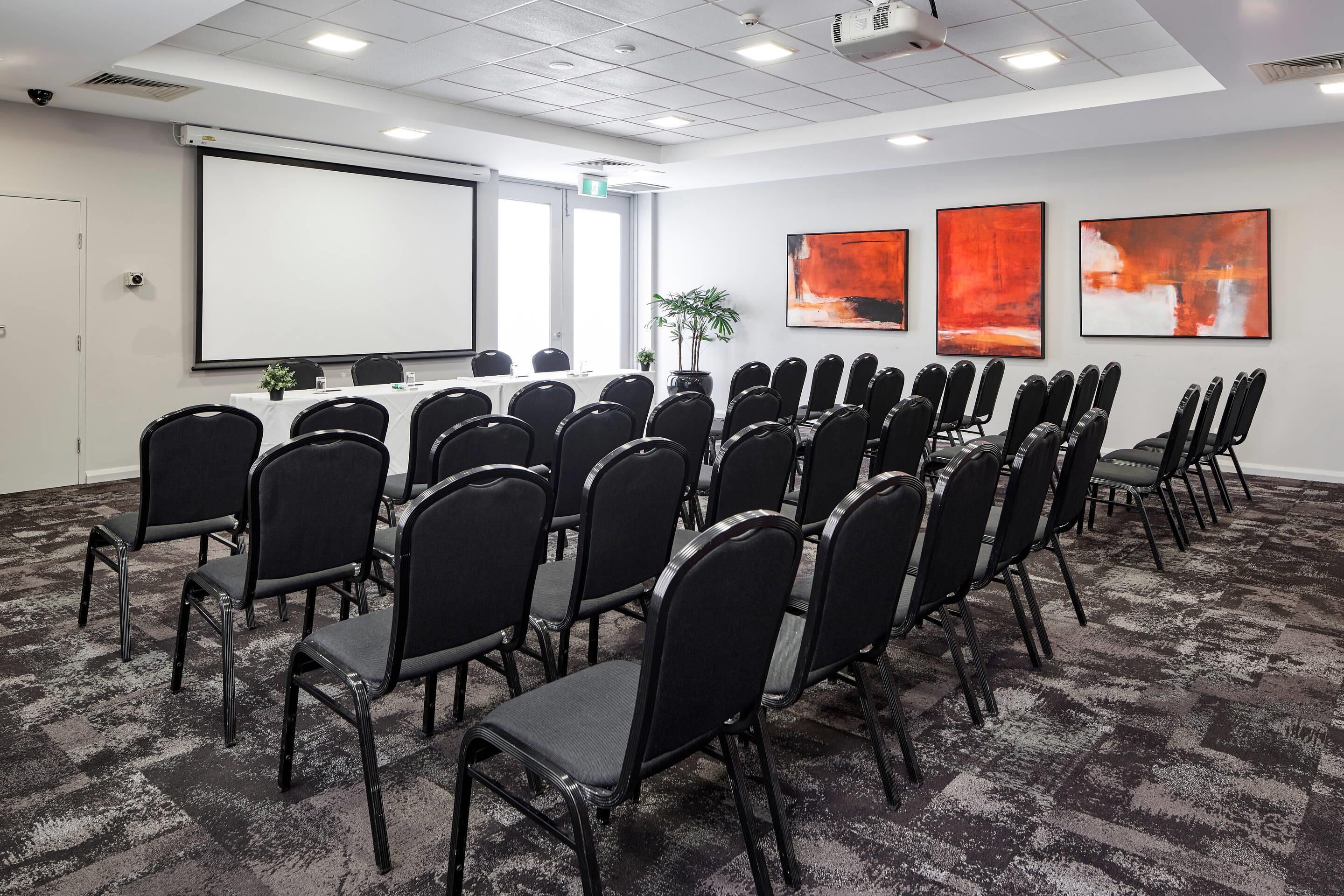 A conference room with rows of chairs, a projector screen, and abstract art on the walls.