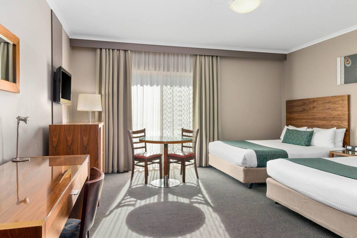 Habitación de hotel con cama, escritorio, silla, televisor y ventana con cortinas.