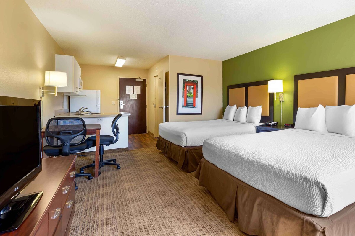 A hotel room with two beds, a desk with a computer, a TV, and a framed picture on the wall.