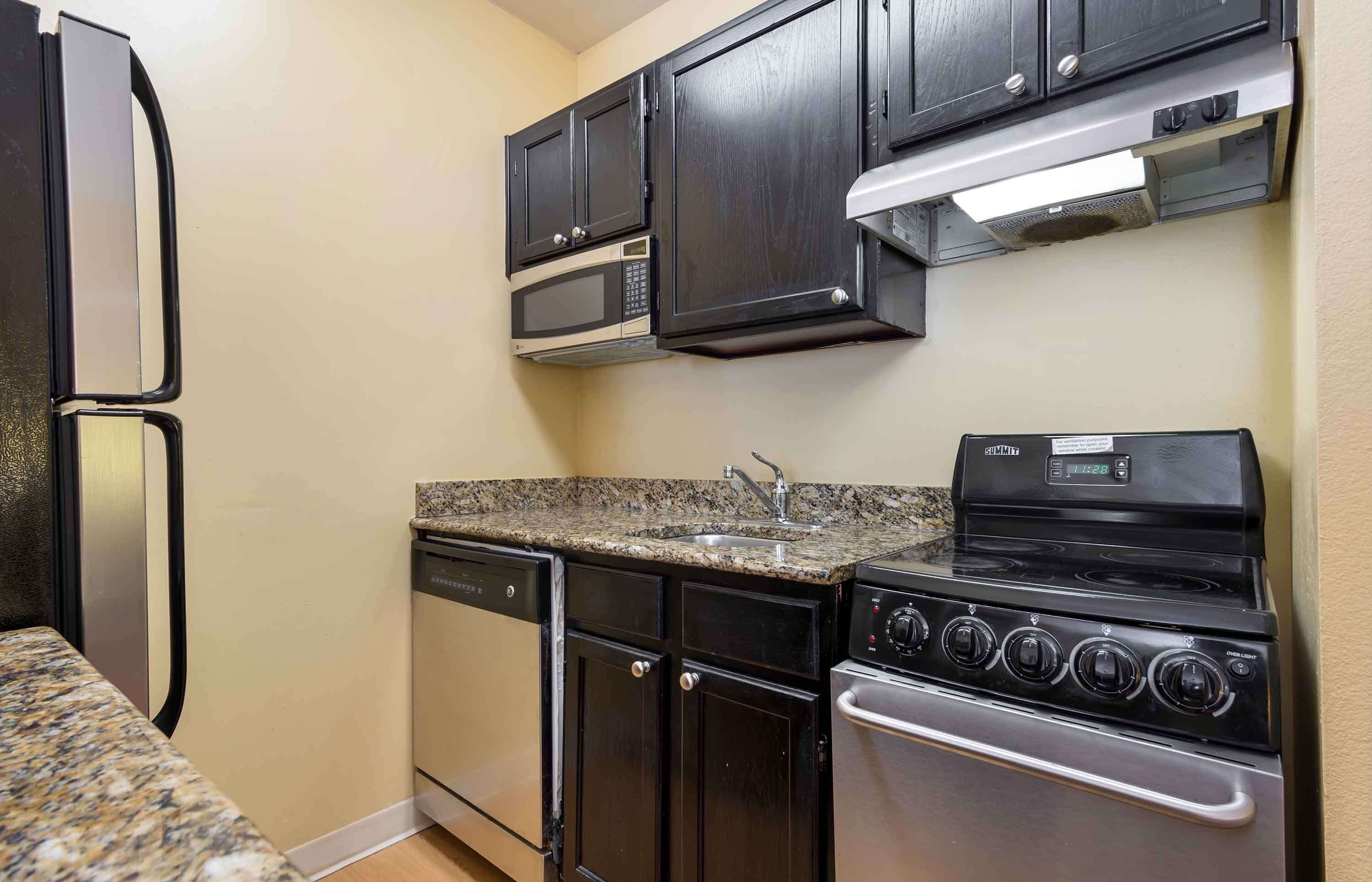 A compact kitchen with dark cabinets, a microwave, a stove, and a dishwasher.