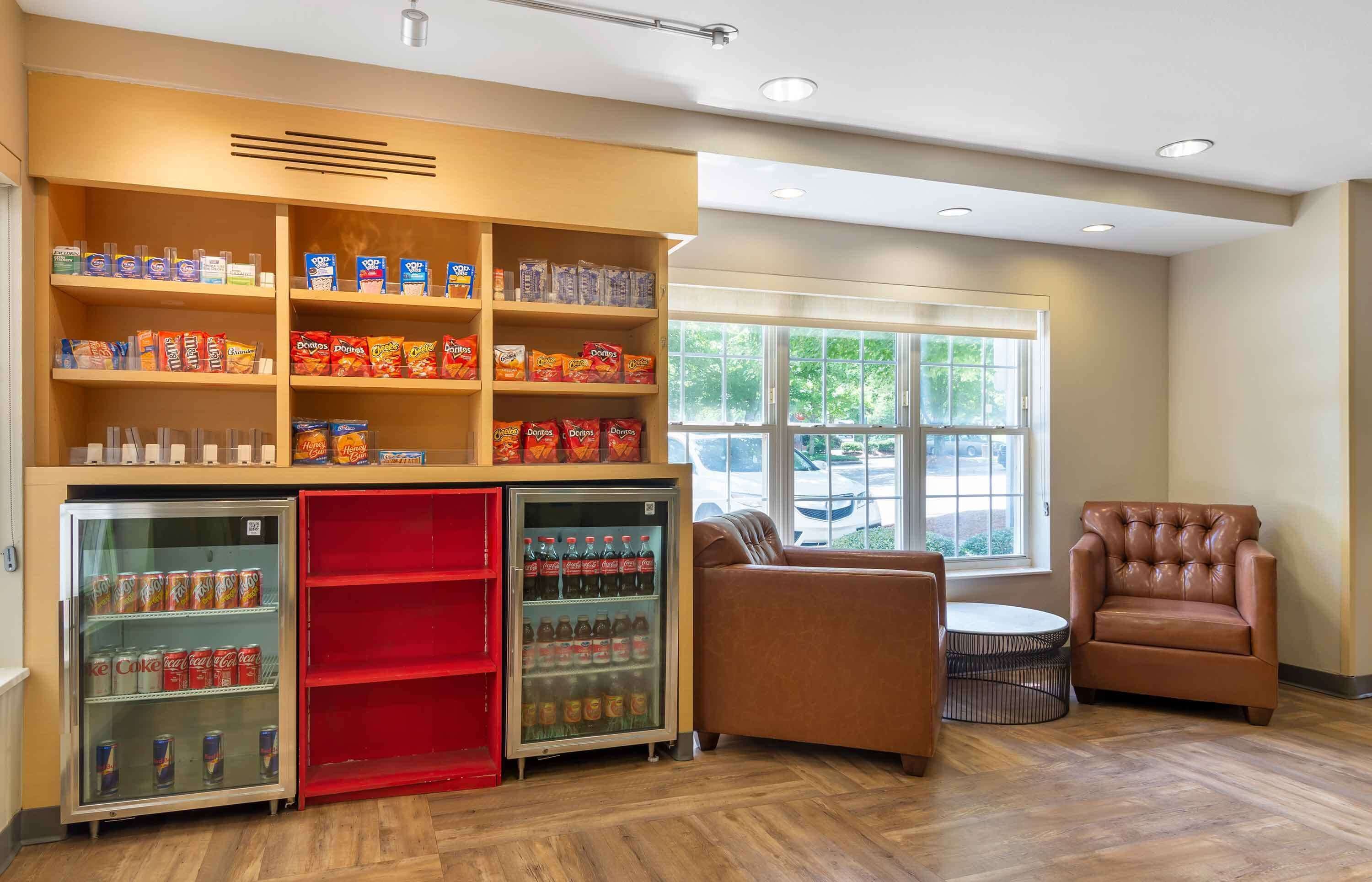 A room with a seating area, a refrigerator stocked with beverages, and shelves with snacks.