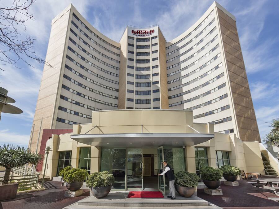 A modern hotel with a curved facade, a central entrance with glass doors, and a red carpet leading to the lobby.