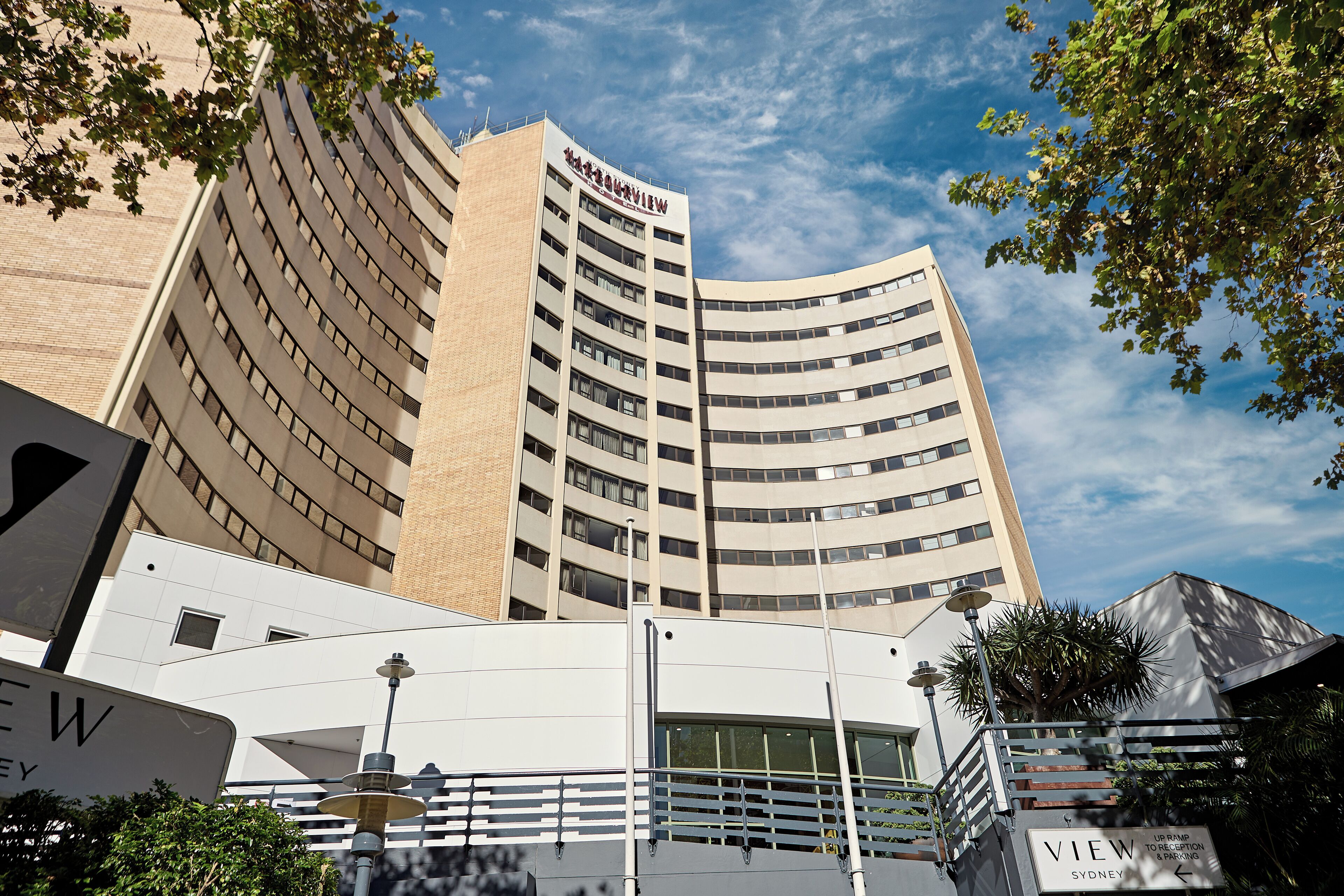 A modern hotel with a curved facade, multiple floors, and a prominent sign reading "View Sydney".