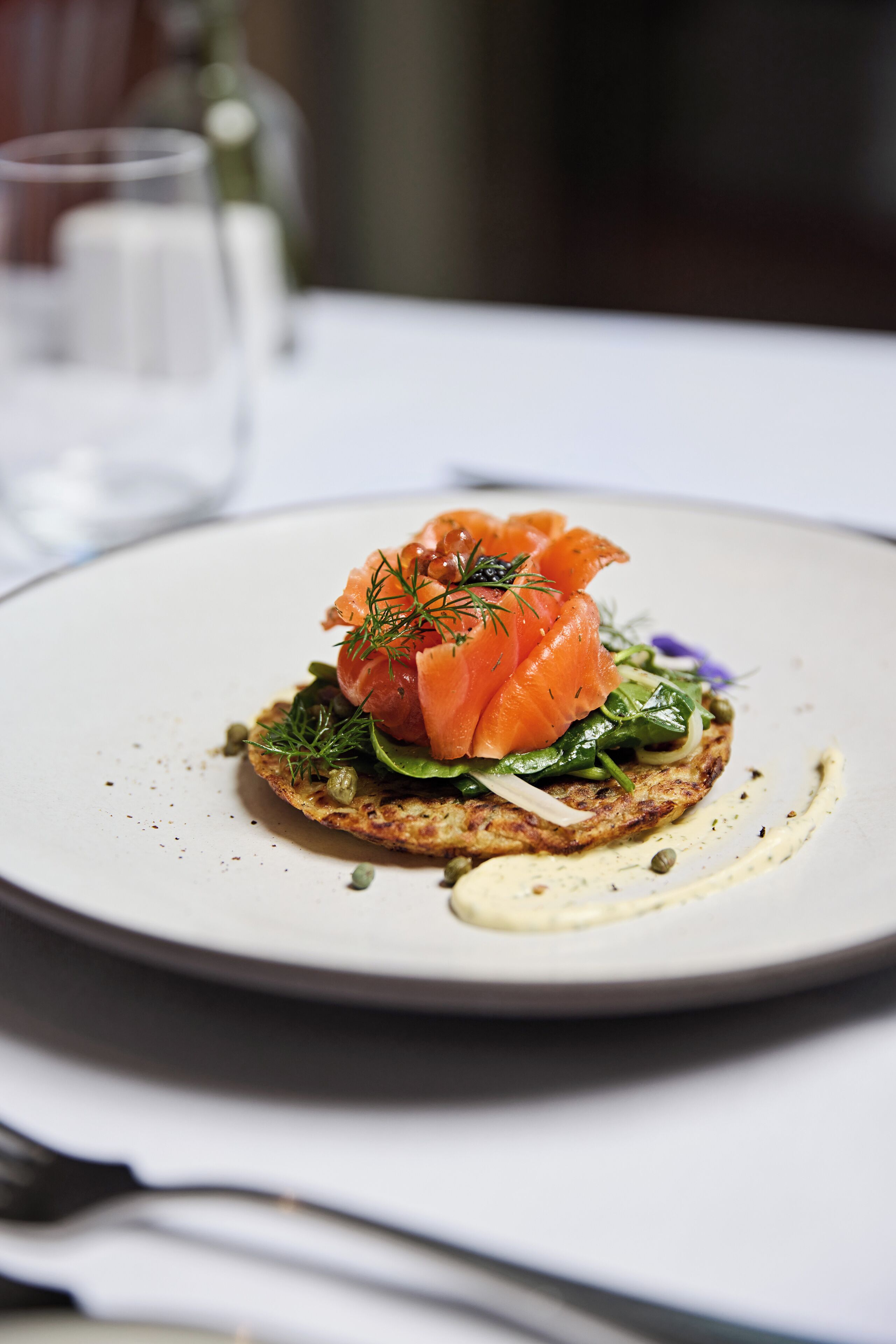 A plate with a dish of smoked salmon, greens, and a creamy sauce on a white plate.