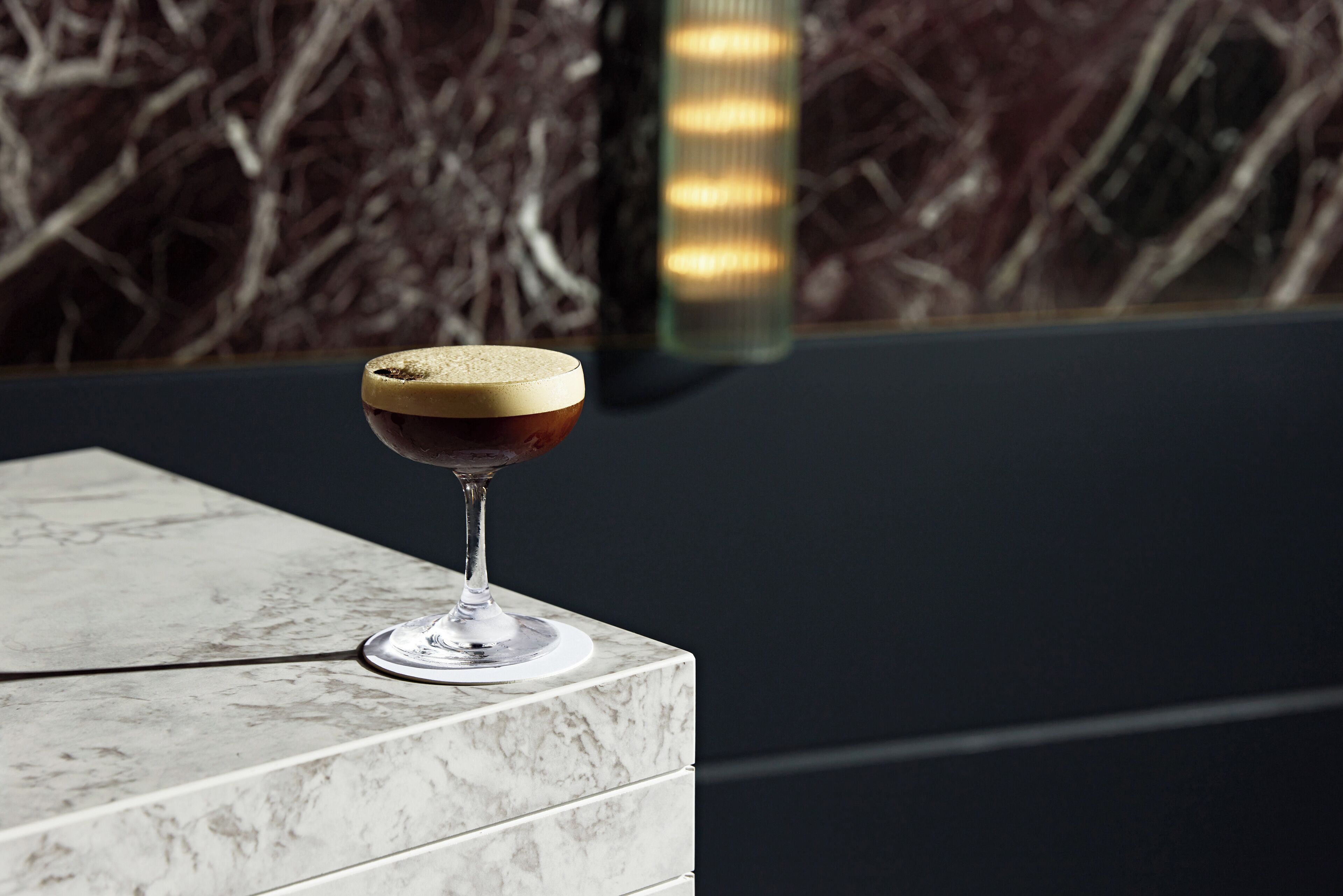 A cocktail glass on a marble surface with a blurred background.