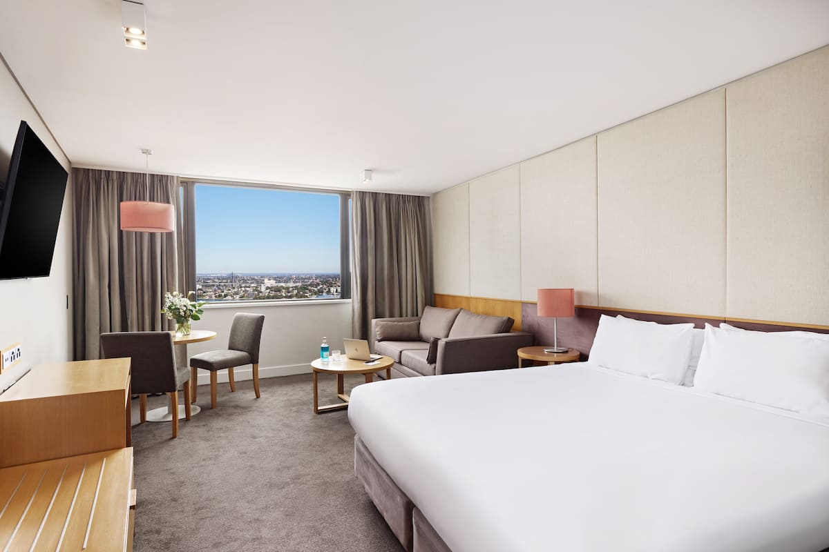 A hotel room with a large bed, a desk, a chair, a small table, and a TV.