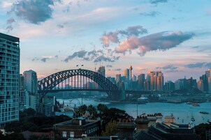 A cityscape with a prominent bridge, high-rise buildings, and a harbor with boats.