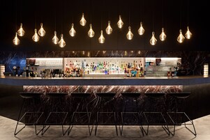 A bar area with a marble countertop, hanging light fixtures, and bar stools.