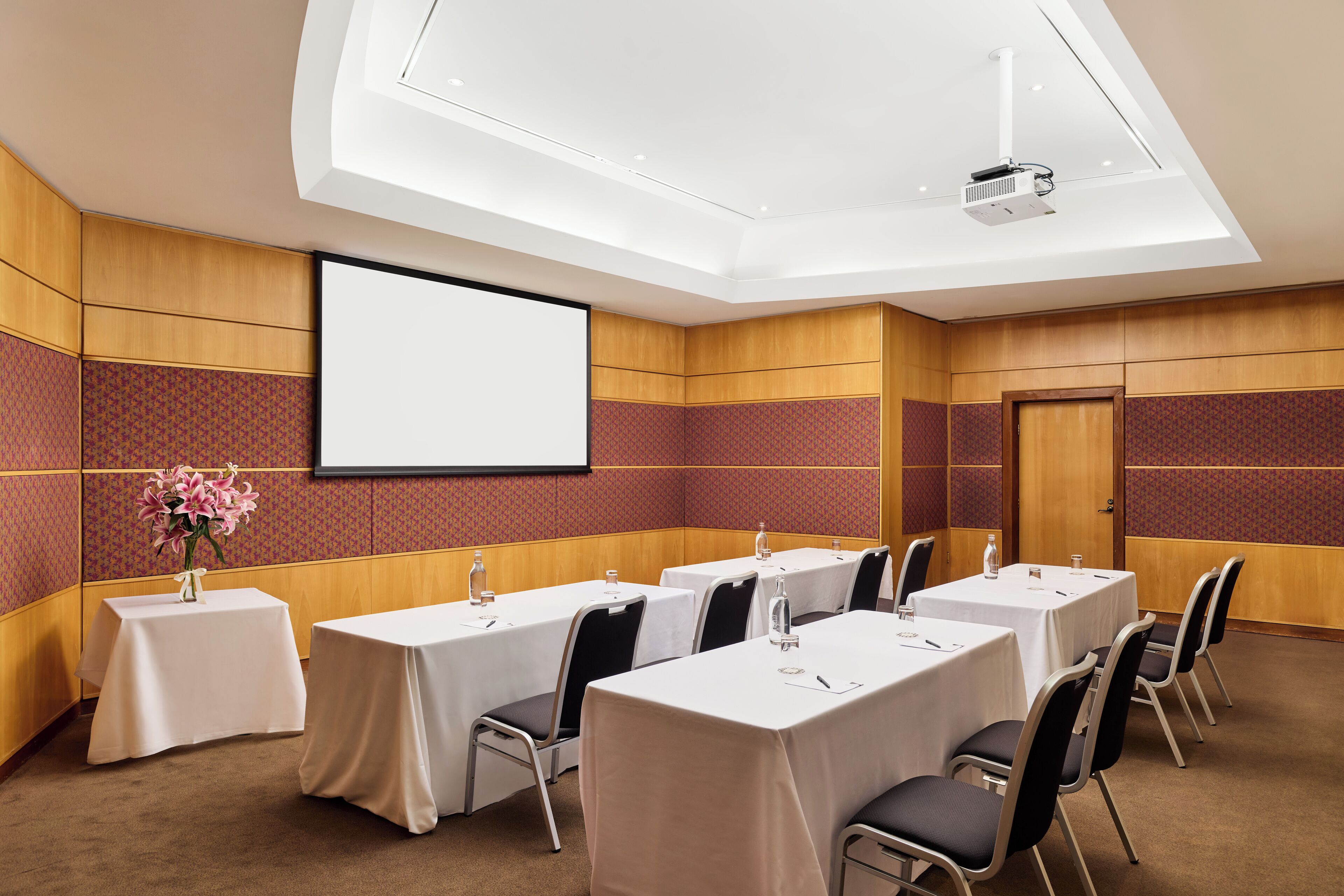 Une salle de conférence équipée de tables, de chaises, d’un écran de projection et agrémentée d’un arrangement floral.