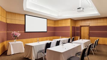 A conference room with tables, chairs, a projector screen, and a floral arrangement.