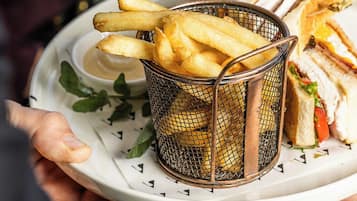 A person holding a plate with a sandwich and a basket of fries.
