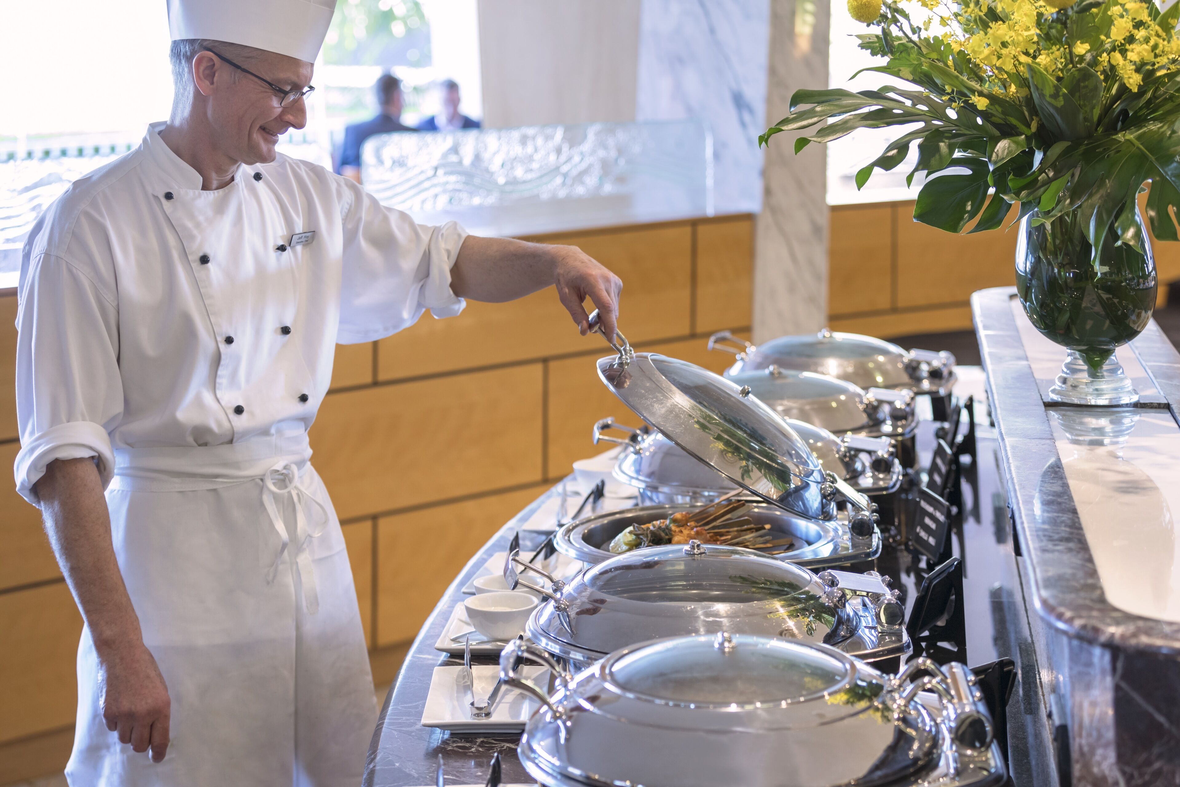 A buffet setup with multiple covered dishes and a chef serving food.