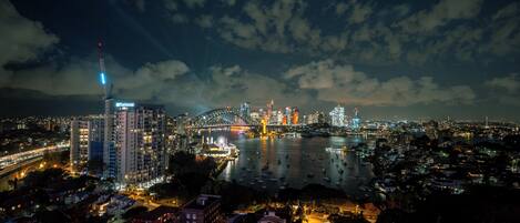 A nighttime cityscape with a prominent bridge, waterfront buildings, and a Ferris wheel.