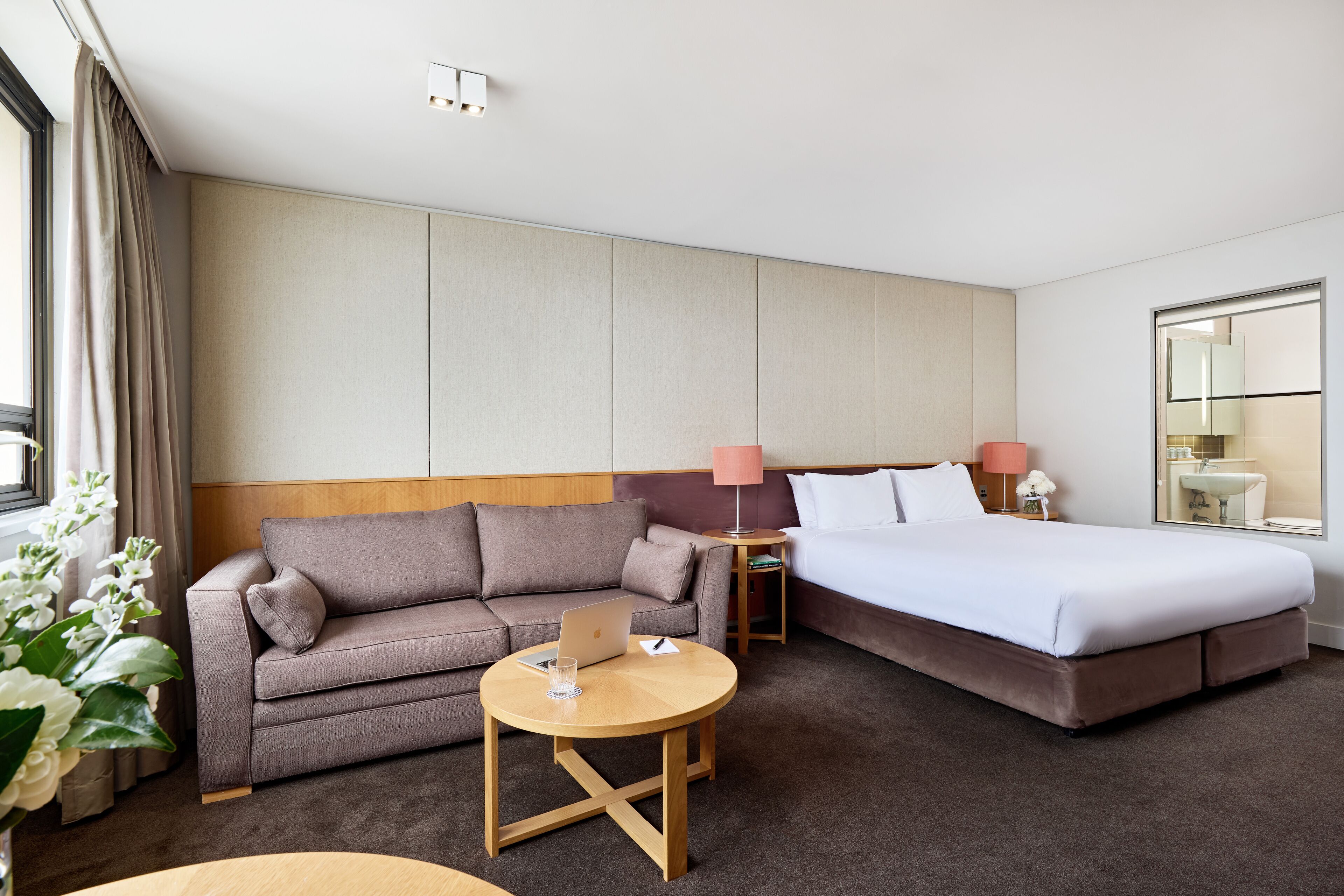 A hotel room with a bed, a sofa, a small table with a laptop, and a lamp.