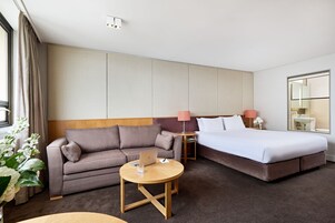 Habitación de hotel con cama, sofá, una pequeña mesa con un ordenador portátil y una lámpara.