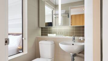 A modern bathroom with a toilet, sink, and a mirror reflecting a bed and a towel rack.