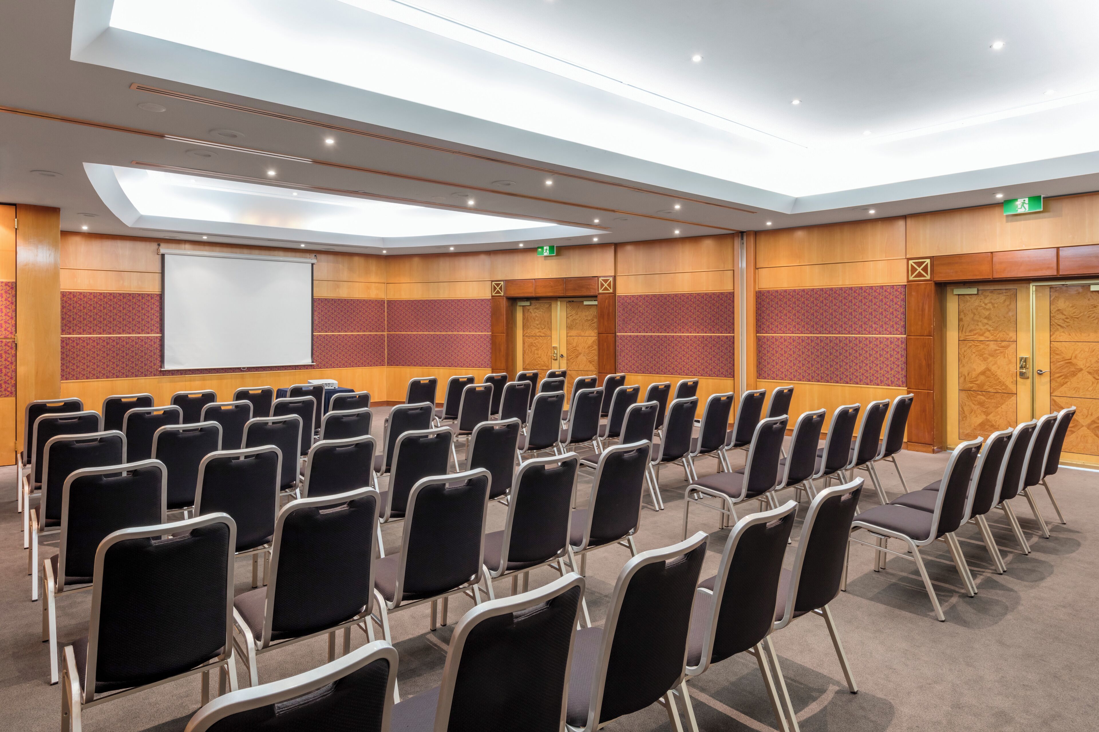 A conference room with rows of chairs, a projector screen, and wooden panel walls.