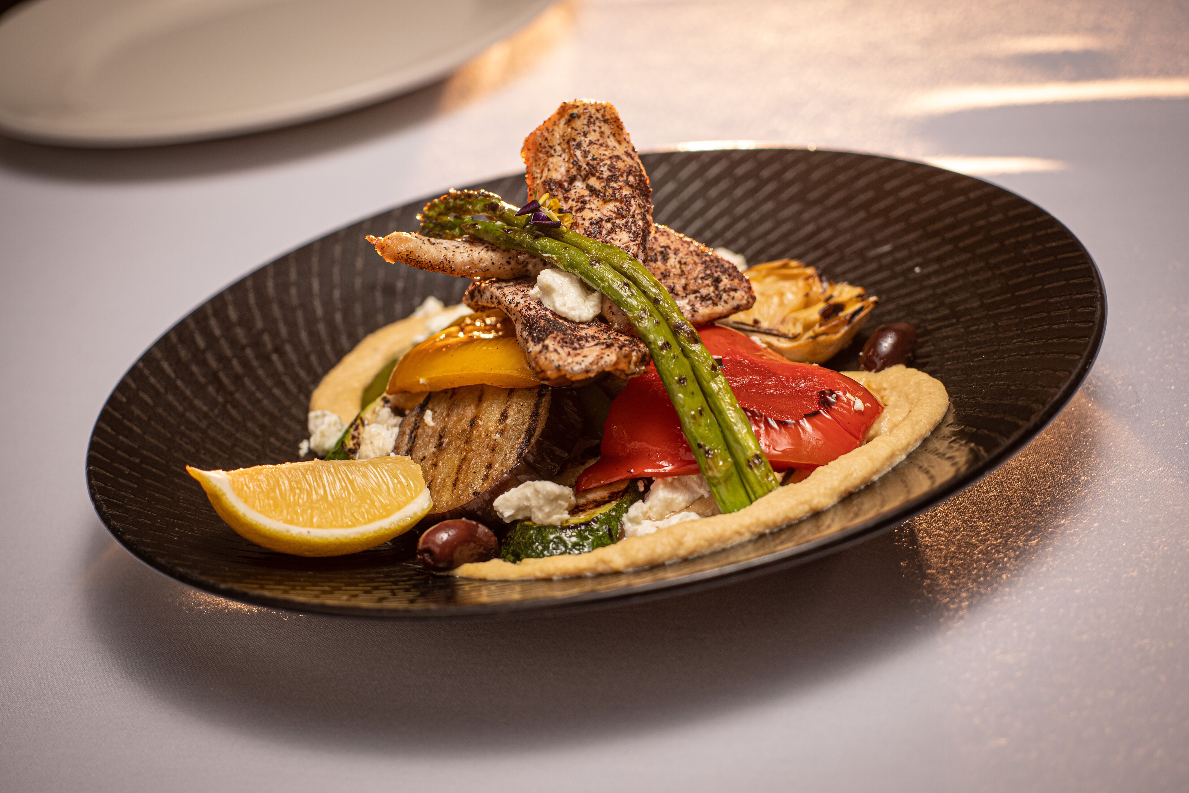 A plate of food with grilled chicken, asparagus, tomatoes, and olives.