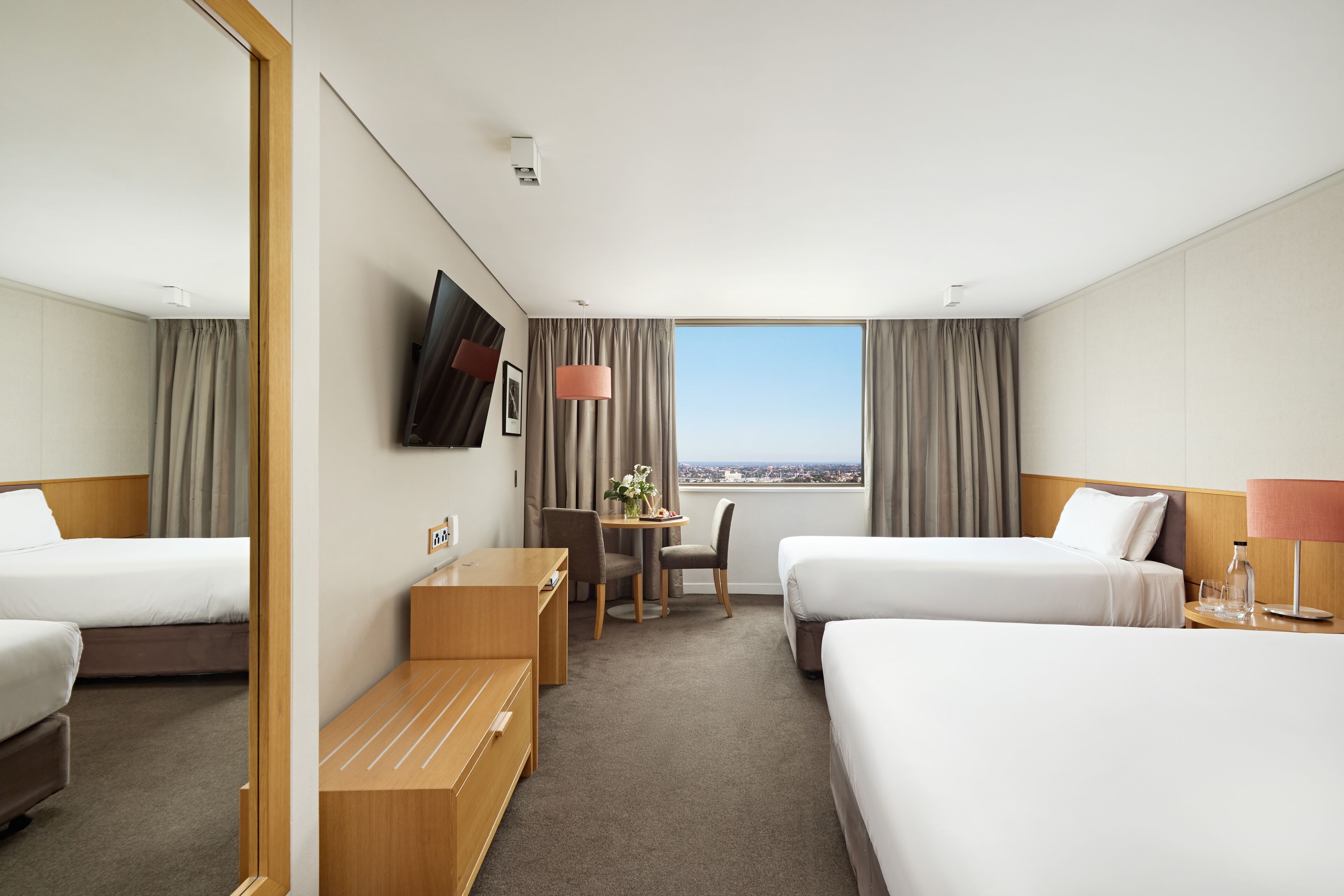 Ett hotellrum med två sängar, ett skrivbord, en stol, en TV och ett fönster med utsikt över staden.
