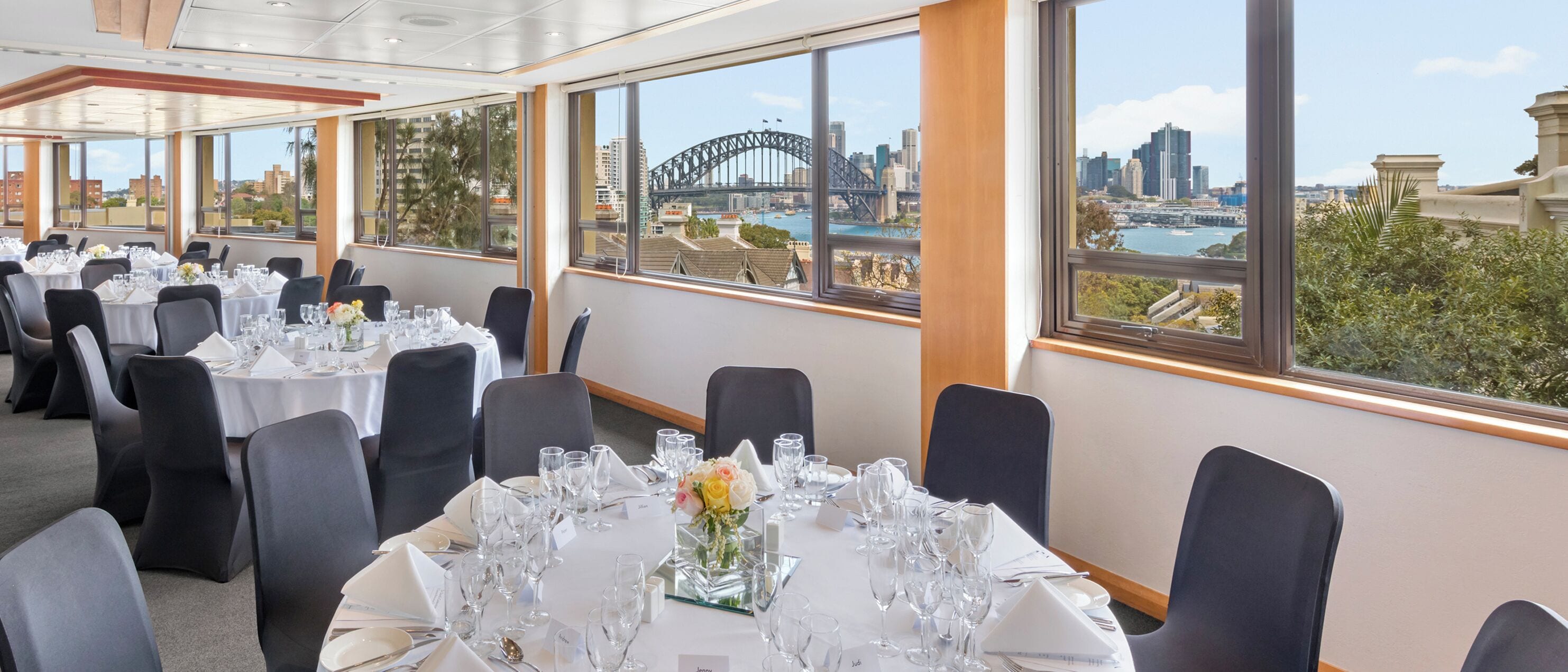 A dining area with tables set for a meal, large windows with a cityscape view including a bridge, and modern interior design.