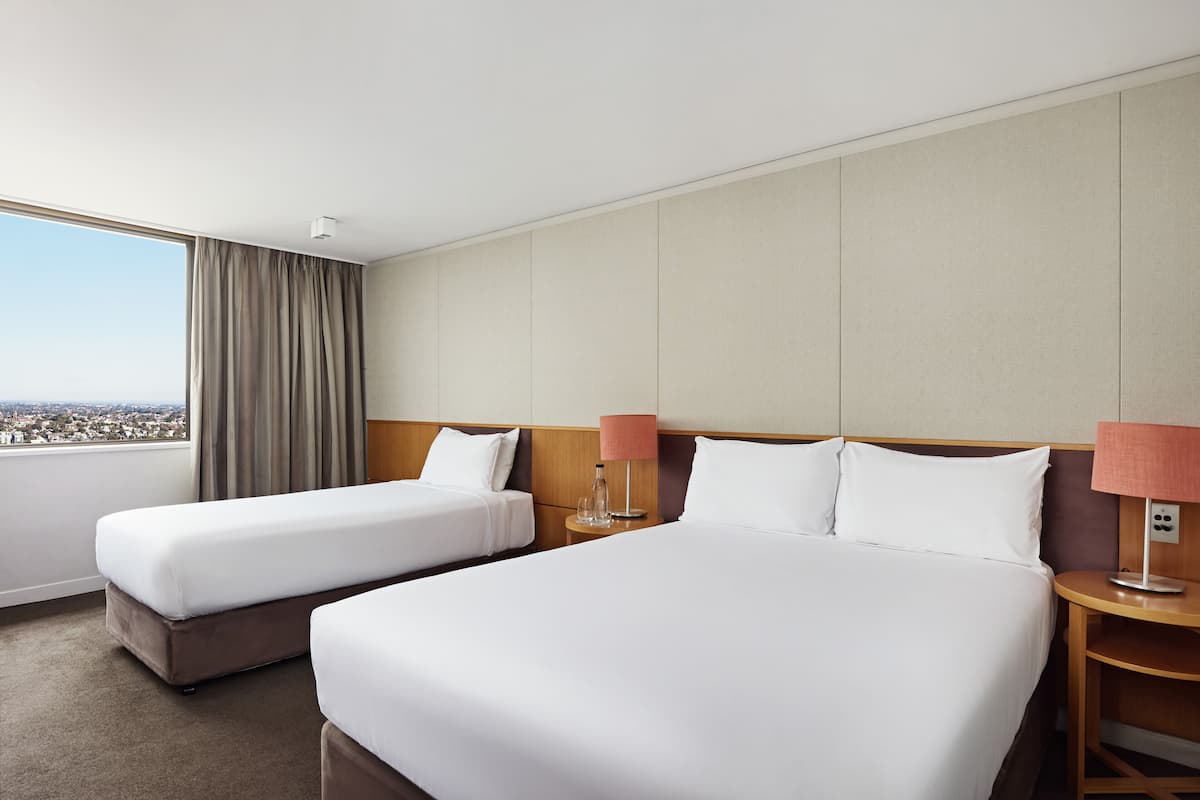 A hotel room with two beds, a large window with a view, and a nightstand with a lamp.