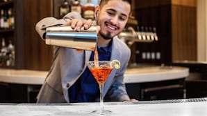 Un barman sirviendo una bebida en una copa de martini, adornada con una rodaja de limón.