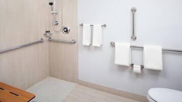A bathroom with a shower, grab bars, a toilet, and a sink.