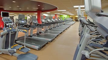 A gym with multiple treadmills and elliptical machines arranged in rows.