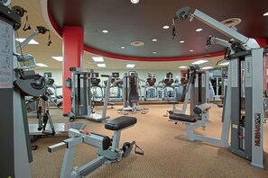 A gym with various exercise machines, mirrors, and red pillars.
