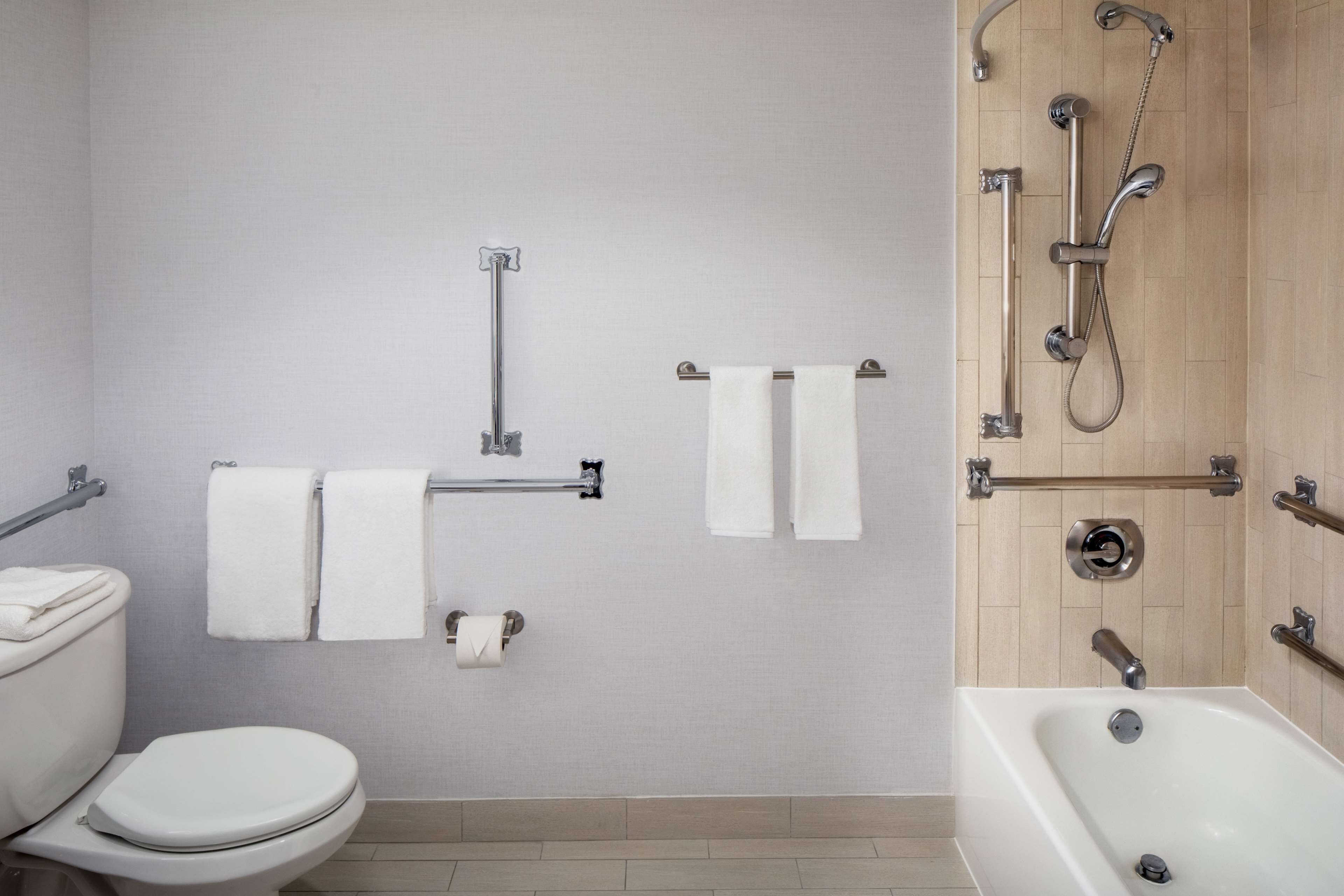 A bathroom with a toilet, two towel racks, a shower with a handheld showerhead, and a bathtub.