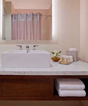 A bathroom with a large rectangular sink, a mirror above it, and a wooden vanity below. There are towels and toiletries on the vanity.