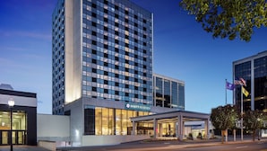 Un hotel moderno con fachada de vidrio, entrada visible y un asta con banderas.