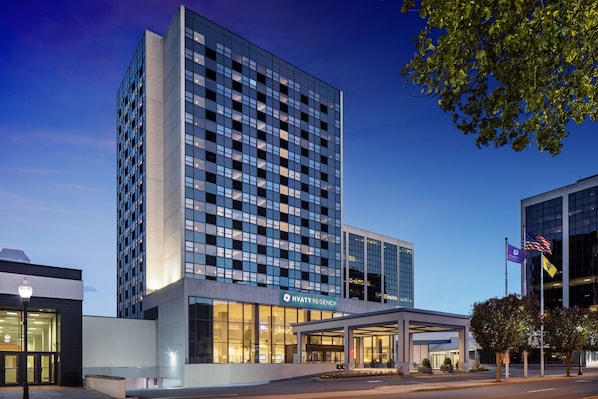 A modern hotel with a glass facade, a visible entrance, and a flagpole with flags.