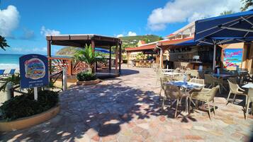 Terraza de restaurante frente a la playa, con suelo de piedra, mobiliario exterior y vistas al océano.