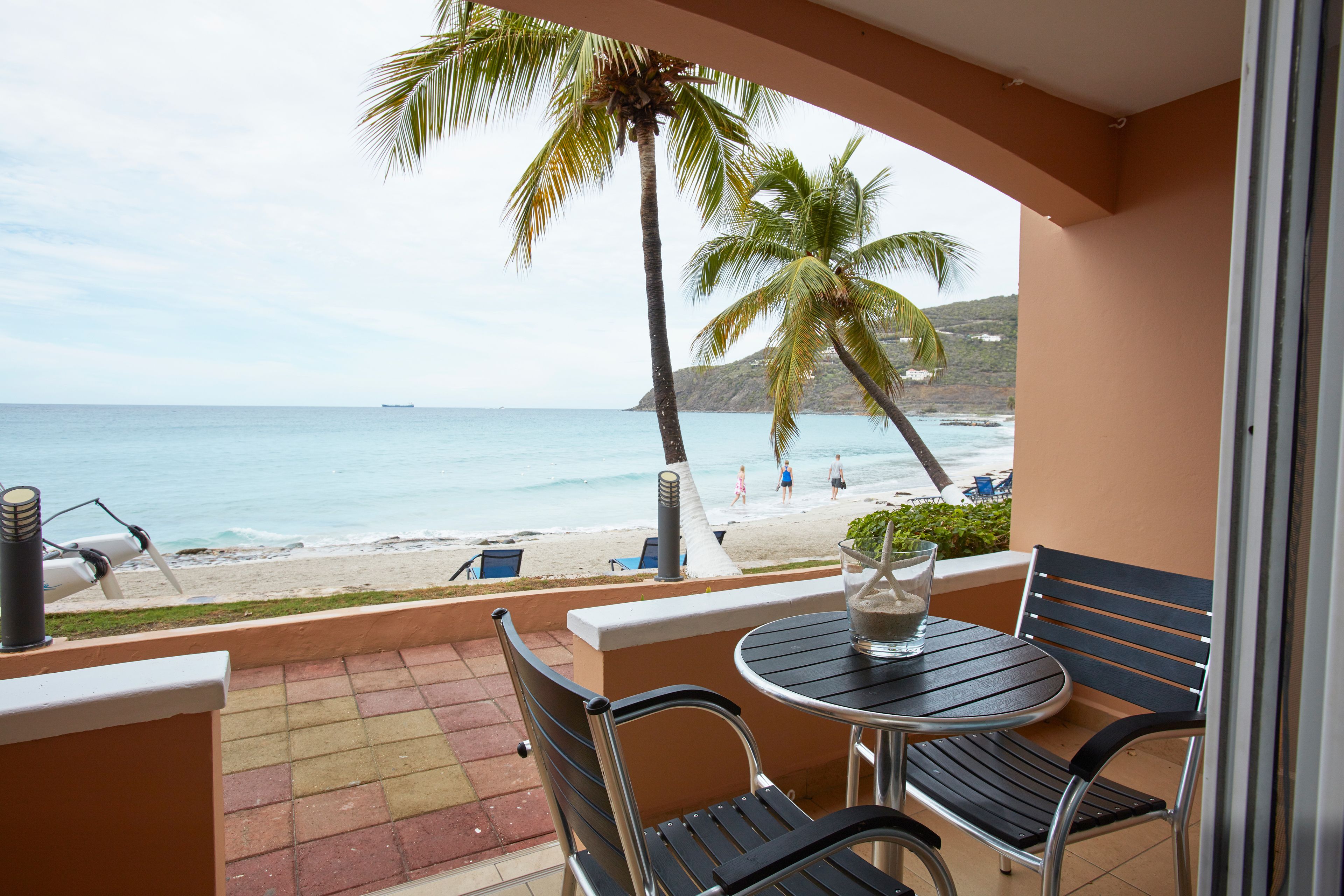 A balcony with a view of the beach, a table with chairs, and a potted plant.