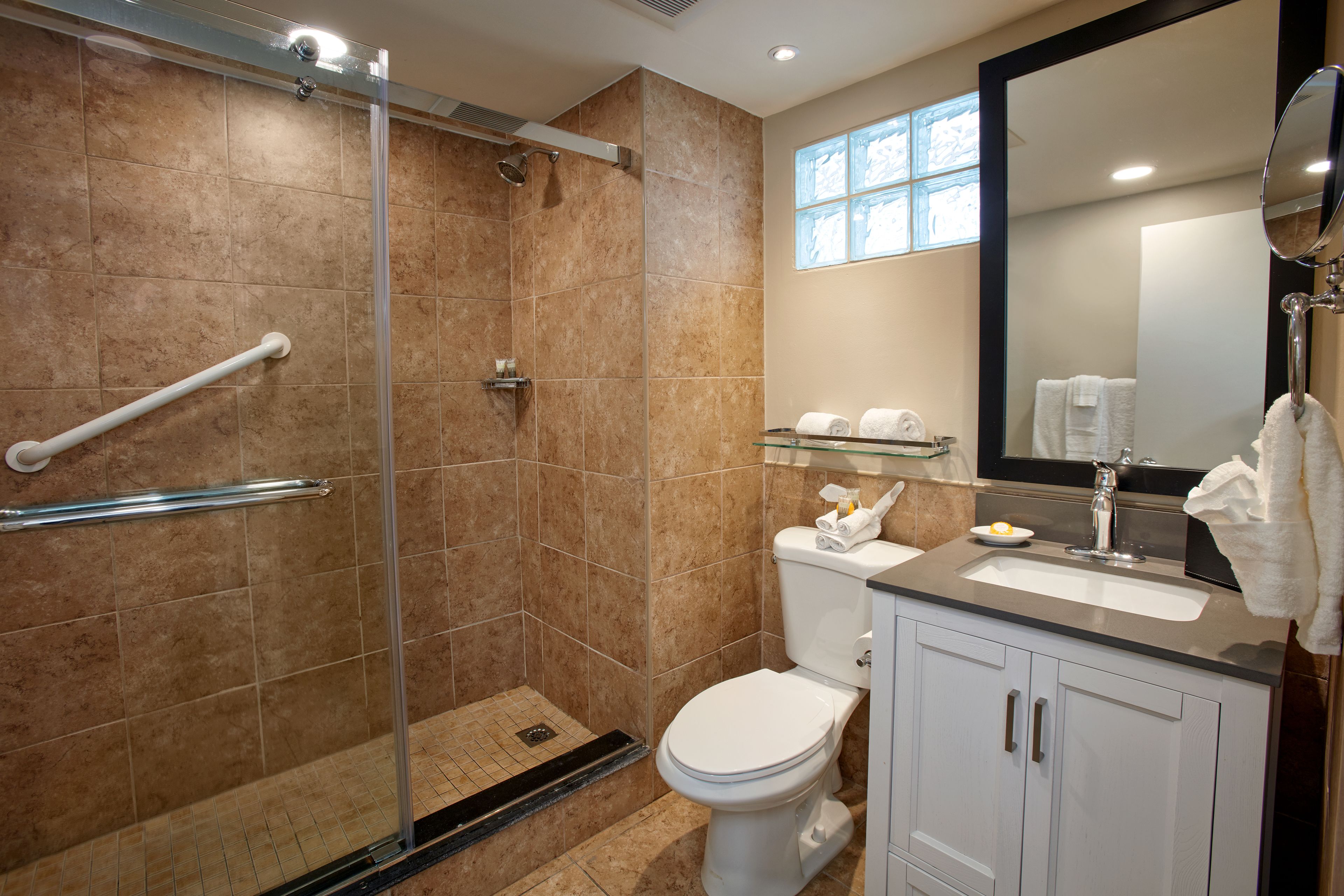 A modern bathroom with a glass shower enclosure, a white toilet, and a vanity with a mirror.