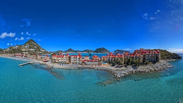 A coastal resort with multiple buildings, clear blue waters, and a mountainous backdrop.