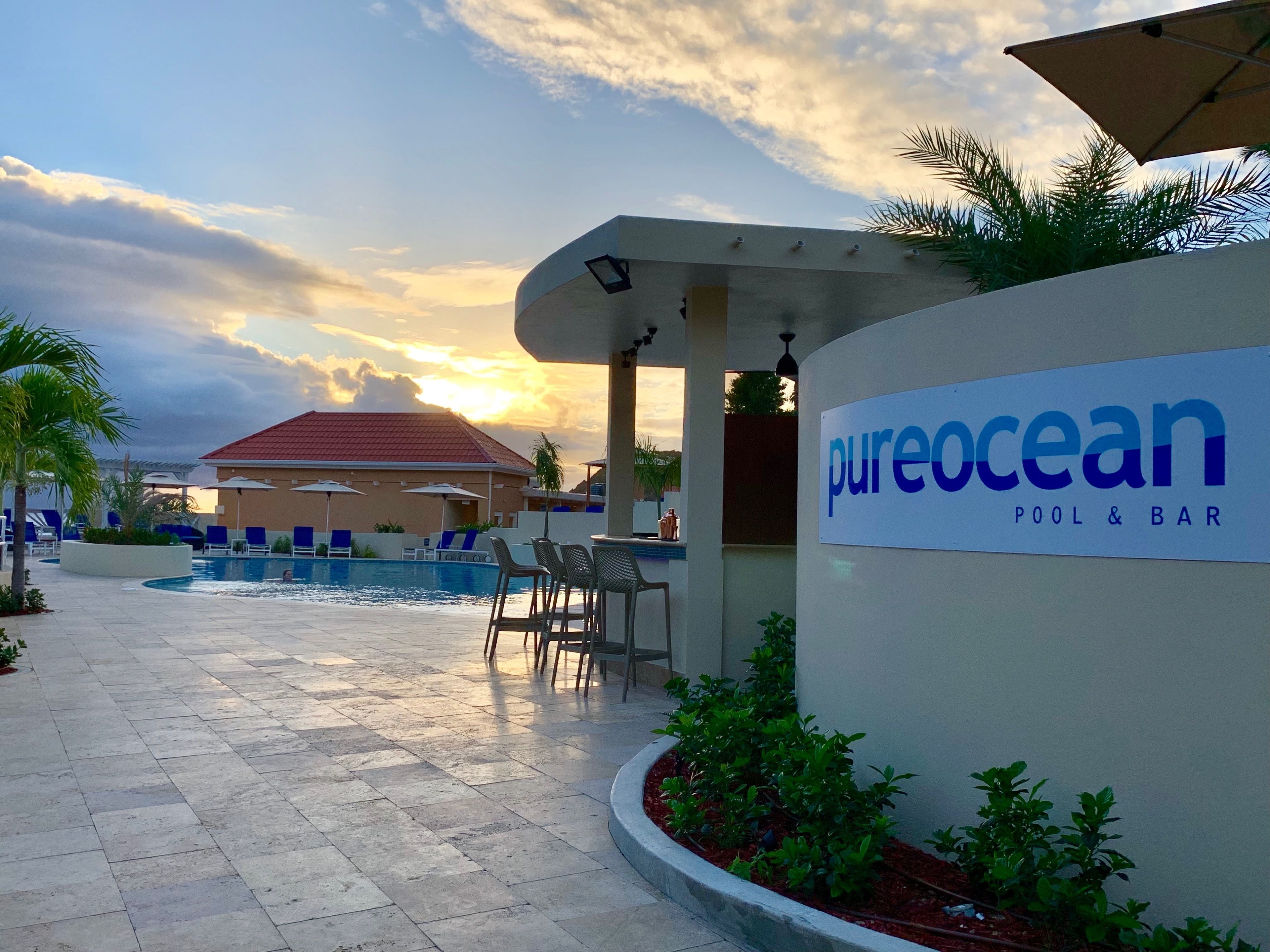 A pool area with lounge chairs and a sign for PureOcean Pool & Bar.