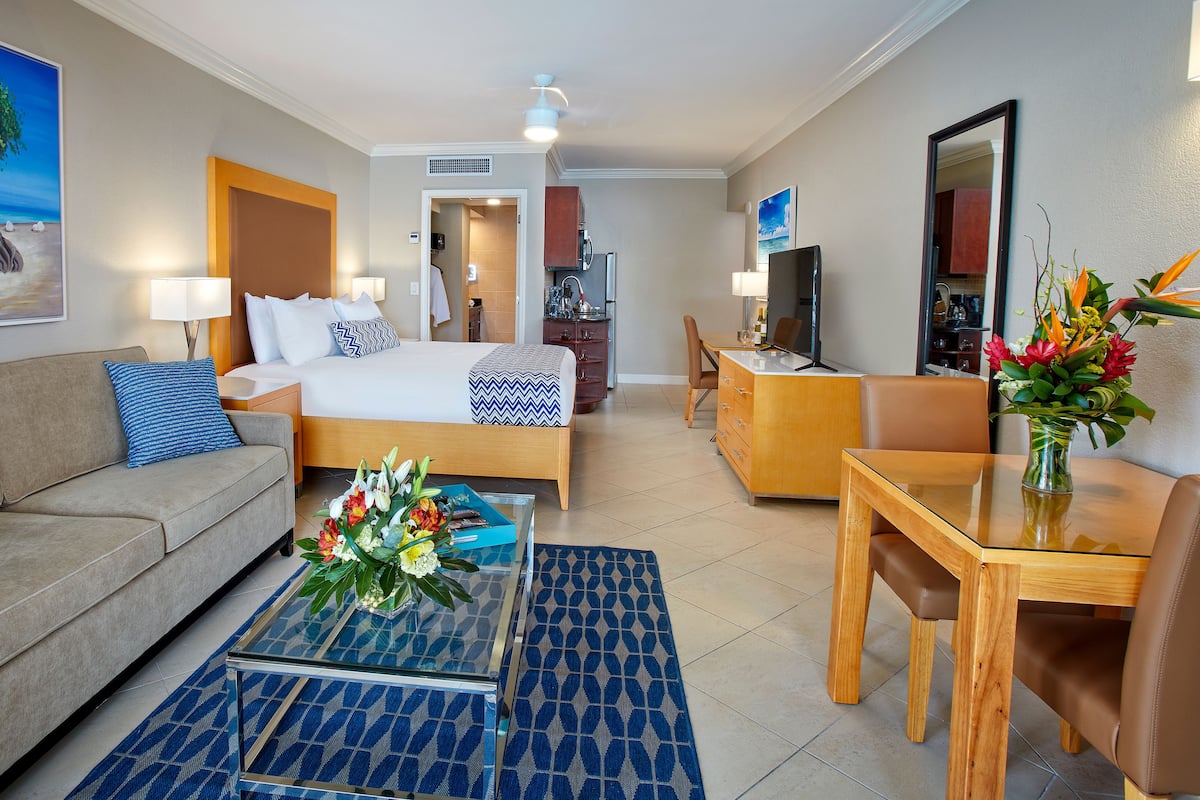 A hotel room with a bed, a sofa, a desk, a TV, and a painting of a tree.