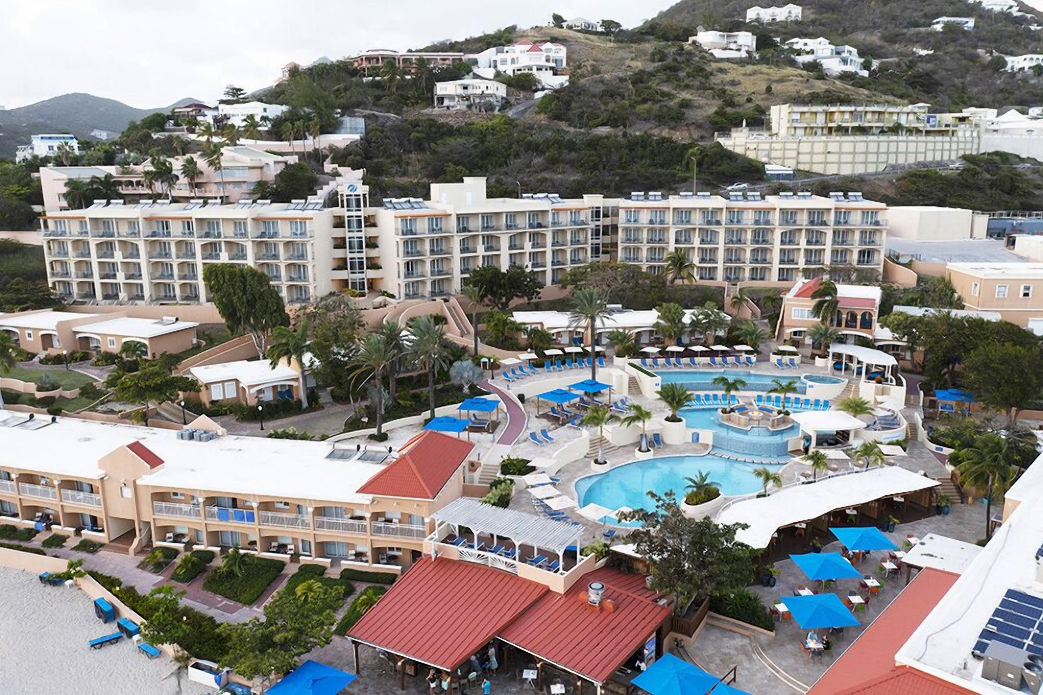 A resort with multiple buildings, a large swimming pool, and a beach area.