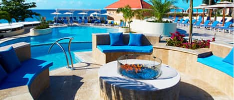 Un espace piscine avec des chaises longues, un foyer extérieur et une vue sur l’océan.