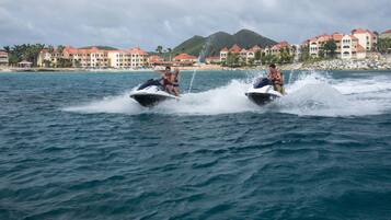 Two people jet-skiing on a body of water with a resort in the background.